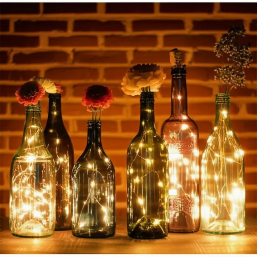 Garrafas de vidro coloridas e decoradas usadas como vasos e luminárias com luzes LED, em um ambiente interno.