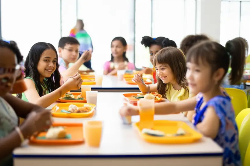 Criancas sorrindo enquanto comem uma refeicao saudavel em uma cantina escolar moderna